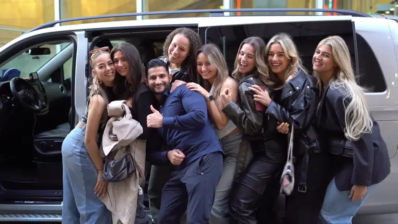 Een groep vriendinnen poseert lachend met hun chauffeur voor de taxibus van Taxi Ous