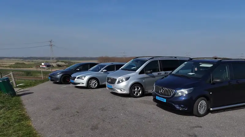 Het wagenpark van Taxi Ous op een rij op de dijk: een sedan, een stationwagen en twee taxibussen